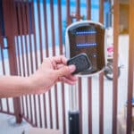 A person uses a key fob to activate an automatic gate opener, with a modern access control system in the background.