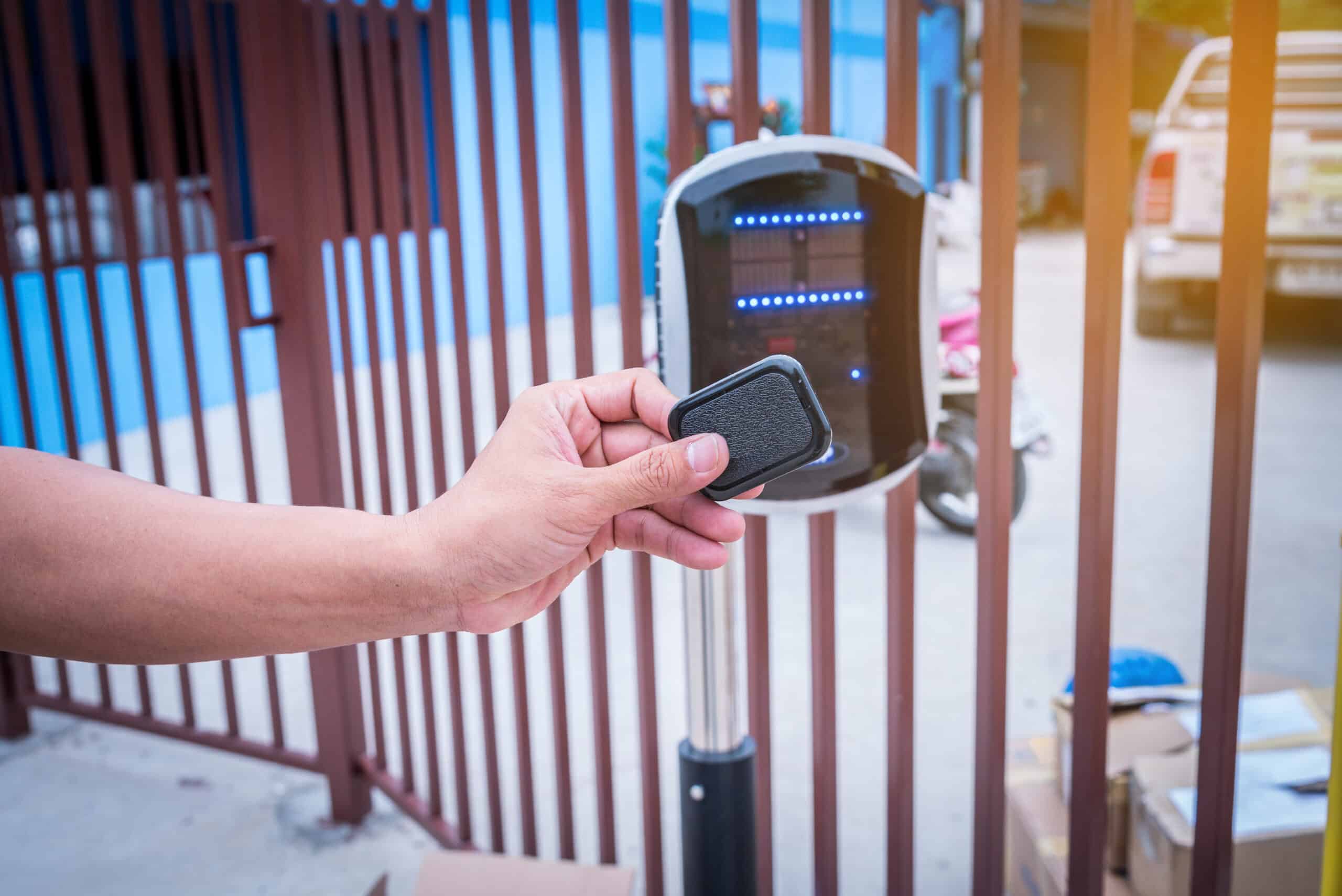 A person uses a key fob to activate an automatic gate opener, with a modern access control system in the background.