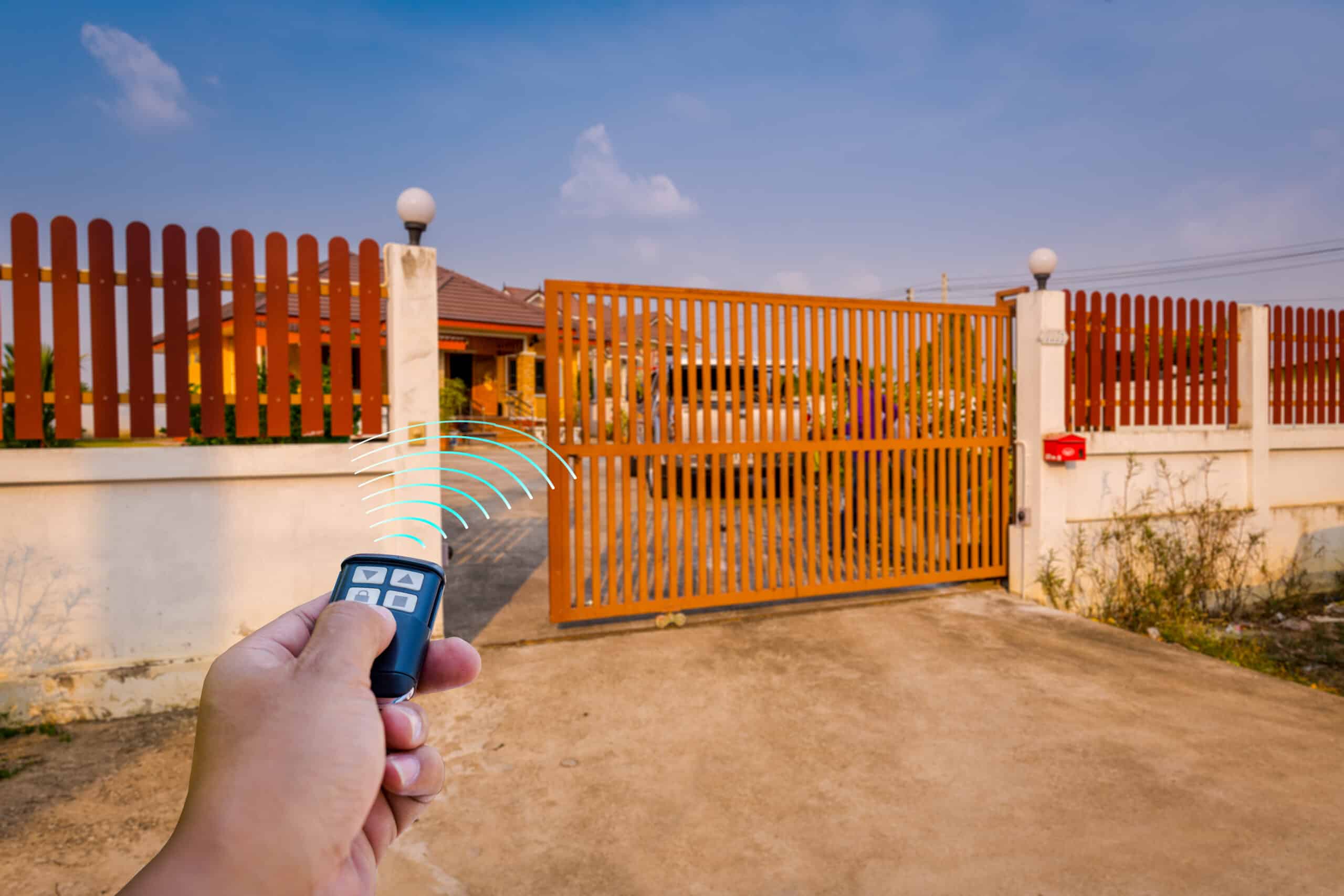 A person uses a remote control to open an automatic sliding gate, leading to a residential property.